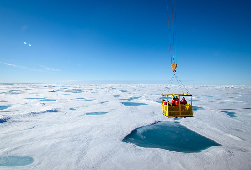 The ice team, consisting of Dr. Eric Collins, Kyle Dilliplaine, and Brian Ulaski, is lowered in a man basket to the ice below from the deck of the Healy.