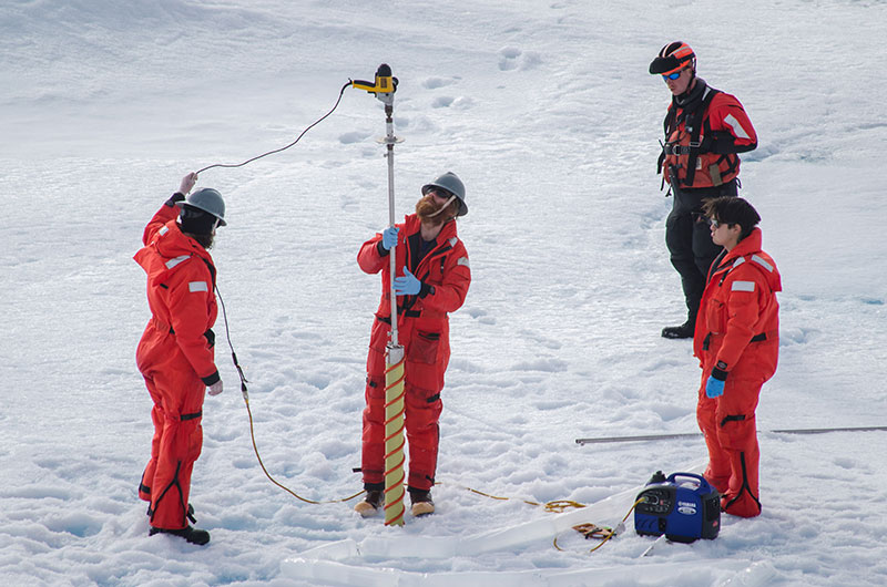 Dr. Eric Collins handles the corer with Kyle Dilliplaine and Brian Ulaski. The collected ice cores can be seen in the plastic tubing at the bottom of the frame.