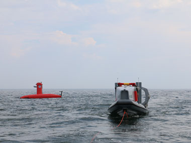 A DriX uncrewed surface vehicle surveys in the distance behind its deployment system.