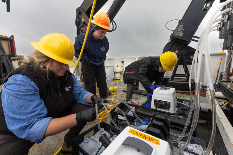 While biological and geological samples were not collected during 2023 Shakedown + EXPRESS: West Coast Exploration engineering-focused dives, water samples were collected using Niskin bottles mounted on remotely operated vehicle Deep Discoverer to ensure the bottles are working properly. Here, expedition biology lead Alexis Weinning (left), geology lead Paige Koenig (center), and benthic biologist Ashley Marranzino process collected water samples using a U.S. Geological Survey pump system on the deck of NOAA Ship Okeanos Explorer. The samples will eventually be analyzed for eDNA (environmental DNA).