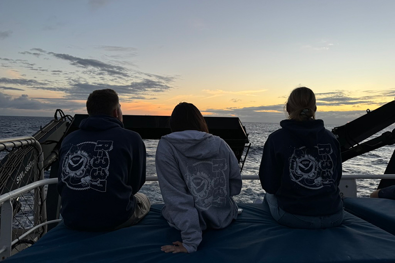 Image of cultural liaison Makoa, explorer in training Anabel, and sample data manager Jennifer out on the blue mats. This is the best place to watch the sunset as the ship has been heading east for the past several days. This prime sunset spot overlooks the fantail of the boat.