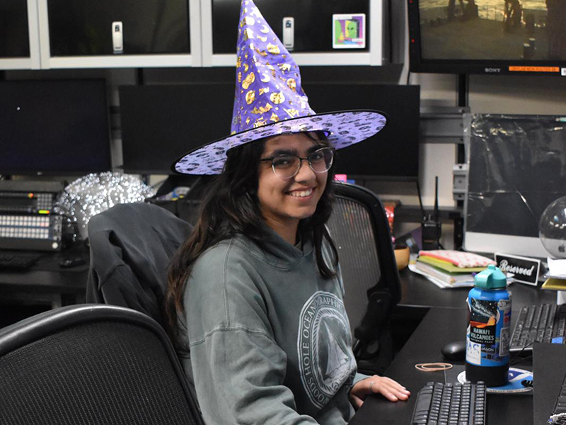 Person wearing a wizard hat in an in the control room, smiling.