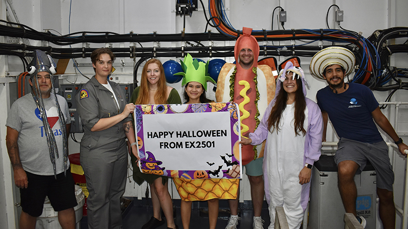 A group of people in Halloween costumes holding a banner indoors.