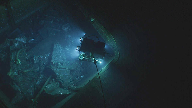 ROV exploring a sunken bomber with bright lights in dark, murky water.